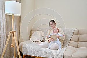 Happy woman mother with infant baby watching in digital tablet while sitting on home sofa in living room