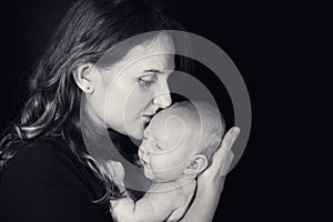 Happy woman mother kissing a newborn baby boy in her arms, black studio background. Mom with a child in her hands