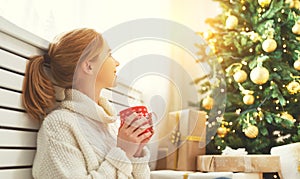 Happy woman with a mug of tea near Christmas tree