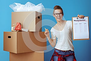 Happy woman near cardboard box showing moving checklist on blue