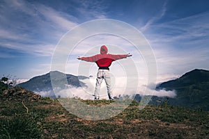 Happy woman with open arms stay on the peak of the mountain cliff edge under light sky enjoying the success, freedom and bright