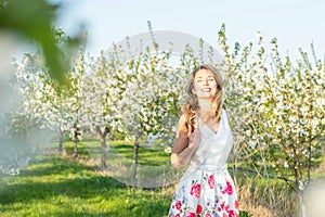 Happy Woman in an orchard at springtime. Enjoying sunny warm day. Retro style dress. Blooming blossom cherry trees