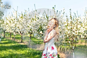 Happy Woman in an orchard at springtime. Enjoying sunny warm day. Retro style dress. Blooming blossom cherry trees