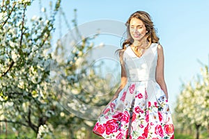 Happy Woman in an orchard at springtime. Enjoying sunny warm day. Retro style dress. Blooming blossom cherry trees