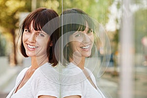 Happy woman outside leaning against reflection in building