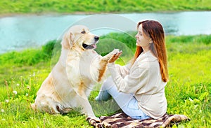 Happy woman owner is training her Golden Retriever dog on grass and giving paw to hand