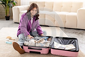 Happy woman packing suitcase in living room