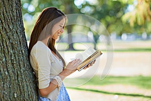 Happy woman, park and reading book for learning, education or leisure in summer. Young person with story, fiction or