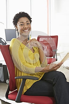 Happy Woman With Pencil And Notepad Sitting On Office Chair