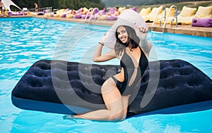 Happy woman with perfect figure sitting on a mattress in the swimming pool and showing thumbs up gesture of good class