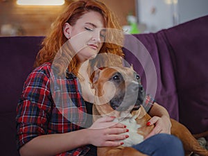 Happy woman petting her merican staffordshire terrier on couch at home in living room