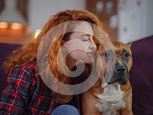 Happy woman petting her merican staffordshire terrier on couch at home in living room