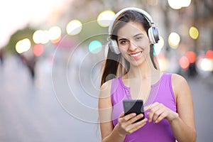 Happy woman with phone and headphone posing in the street