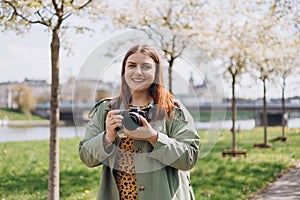 Happy Woman photographer with camera taking pictures on park background. Hobby, lifestyle, travel, people concept. 30s