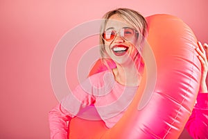 Happy woman in pink heart shaped sunglasses holding pink inflatable ring toy for the pool