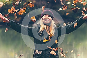 Happy Woman playing with autumn leaves raised hands