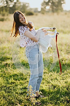 Happy woman playing with cute active white puppy in warm light in summer meadow. Funny moments