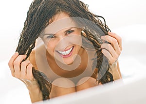 Happy woman playing with wet hair in bathtub