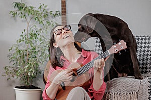 happy woman plays the ukulele and rests at home with her dog. a successful female musician gives music lessons online.