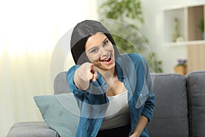 Happy woman pointing at camera on a couch at home