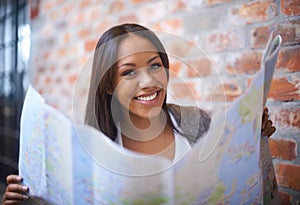 Happy woman, portrait and reading map for travel, immigration or commute by a brick wall. Face of female person, tourist