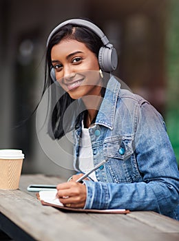 Happy woman, portrait and student writing with headphones for audio, learning or music at outdoor cafe. Young female