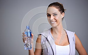 Happy woman, portrait and water bottle in fitness for hydration on a gray studio background. Face of thirsty female
