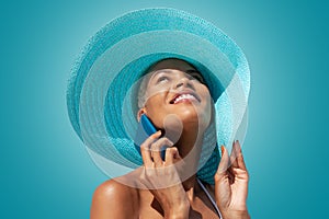 Happy woman portrait wearing blue sun hat and using mobile phone, isolated on turquoise bright background. Concept of summer beach