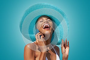 Happy woman portrait wearing blue sun hat and using mobile phone,  on turquoise bright background. Concept of summer beach