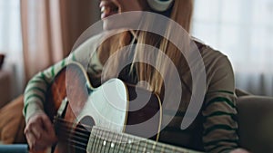 Happy woman practicing guitar playing in earphones at apartment close up.