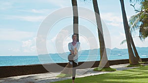 Happy woman is practicing yoga, balance exercise, stretching leg, warrior pose, on the beach, beautiful background, nature sounds