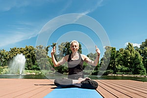 happy woman practicing yoga in lotus pose on yoga mat near river
