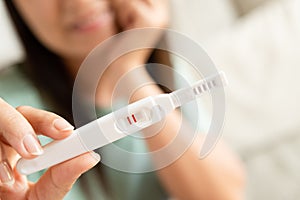 Happy woman with pregnancy test positive result, focus on foreground 2 stripes