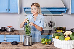 Happy woman putting ingredients into blender to make healthy smoothie for breakfast, cooking vegetables preparing salad