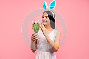 Happy woman in rabbit ears flower with painted eggs, traditional holiday, in the studio on a pink background