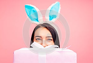 Happy woman in rabbit ears with a gift in her hands, a traditional holiday, in the studio on a pink background