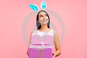 Happy woman in rabbit ears with gifts in her hands, traditional holiday, in the studio on a pink background, easter gift