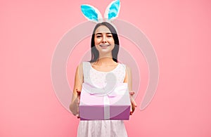 Happy woman in rabbit ears gives a gift, a traditional holiday, in the studio on a pink background, an easter gift