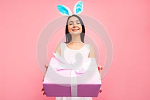Happy woman in rabbit ears gives a gift, a traditional holiday, in the studio on a pink background, an easter gift