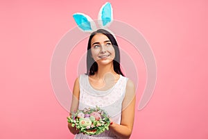 Happy woman in rabbit ears holding a green wreath with colored eggs, a traditional holiday, Easter mood