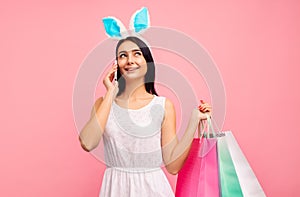 Happy woman in rabbit ears with shopping bags in her hands, talking on the phone, easter mood