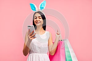 Happy woman in rabbit ears with shopping bags in her hands, typing a message on the phone, easter mood