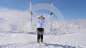 Happy Woman raises her downhill skis on the mountaintop