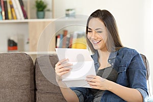 Happy woman reading a letter on a couch at home