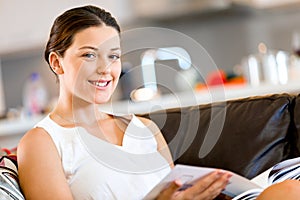 Happy woman reading a magazine sitting on a sofa