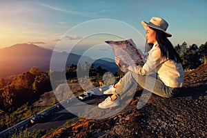 Woman reading a map siting on green grass meadow on top of mountain and enjoying nature ,sunrise in winter