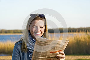 Happy woman reading newspaper near lake. fine news concept.