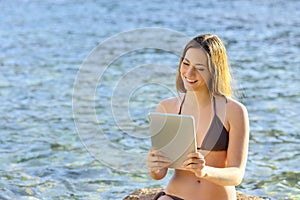 Happy woman reading a tablet reader on the beach seaside