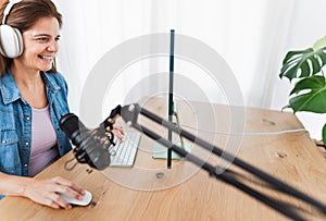 Happy woman recording a podcast using computer and microphone from home studio