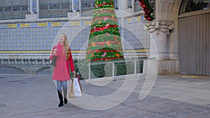 Happy woman in a red coat with shopping bags and a coffee.